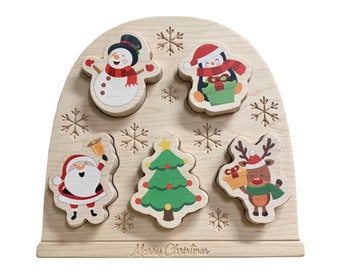 Op de afbeelding: Houten kerstpuzzel met vijf stukken met een sneeuwpop, een pinguïn, de kerstman, een kerstboom en een rendier. De puzzelstukken passen in een houten boog met sneeuwvlokken en de woorden "Prettige Kerst".