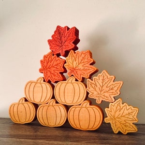 May include: A stack of wooden fall-themed blocks featuring pumpkins and maple leaves in shades of orange, red, and brown.