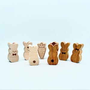 May include: A set of wooden bunny and carrot shaped toys. The bunnies are painted in natural wood tones and have black eyes and bowties. The carrot is painted in a natural wood tone.
