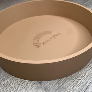 May include: A large, round, beige sensory play tray with the words "Sensory Play" embossed on the bottom.