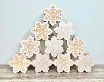 May include: A set of nine wooden snowflake ornaments in a triangular arrangement. The snowflakes are a light brown color with a darker brown outline.
