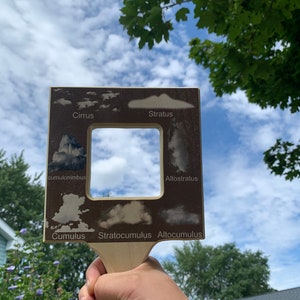 May include: A wooden cloud identification tool with a cutout window. The tool features illustrations of different types of clouds, including cumulus, stratus, cirrus, cumulonimbus, altostratus, altocumulus, and stratocumulus.
