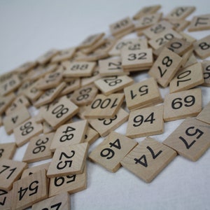 May include: A pile of wooden tiles with numbers printed on them. The tiles are scattered on a white surface.