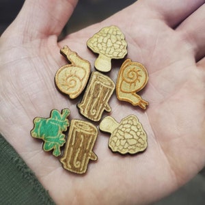 May include: A collection of wooden cutouts featuring a frog, mushrooms, and snails. The cutouts are painted in shades of green, brown, and white.