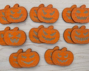May include: Ten orange wooden pumpkin ornaments with carved jack-o'-lantern faces. The pumpkins are arranged in three rows on a light wood surface.