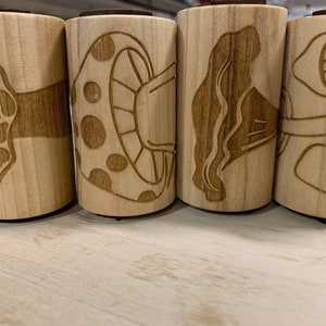 May include: Four wooden rolling pins with different mushroom designs carved into them. The designs include a mushroom with a spotted cap, a mushroom with a wavy cap, a mushroom with a smooth cap, and a mushroom with a textured cap.