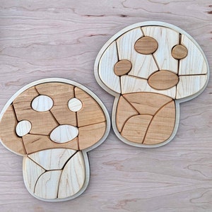 May include: Two wooden mushroom-shaped puzzles with a light brown and white color scheme. The puzzles are made of multiple pieces that fit together to form the shape of a mushroom.