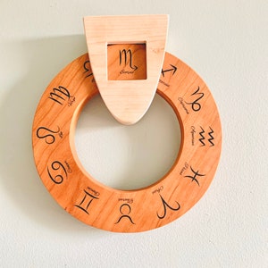 May include: A wooden zodiac wheel with the astrological signs engraved on it. The wheel is mounted on a wall with a separate wooden piece that displays the Scorpio sign.