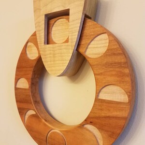 May include: A wooden wall hanging with a circular design featuring various phases of the moon. The moon phases are carved into the wood and are surrounded by a larger circle of wood. The top of the piece features a square cutout with a circle inside.
