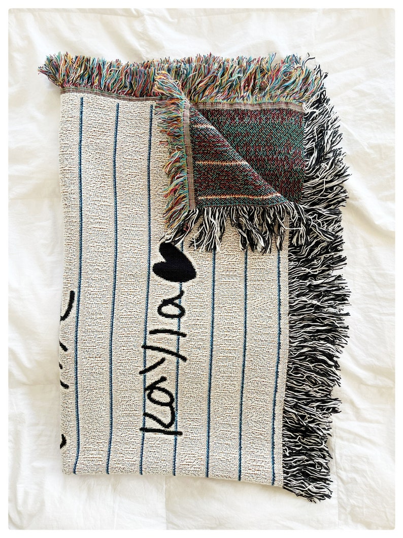 May include: A white woven throw blanket with black stripes and the words "I love you" written in black. The blanket has a fringe border and is folded in half.