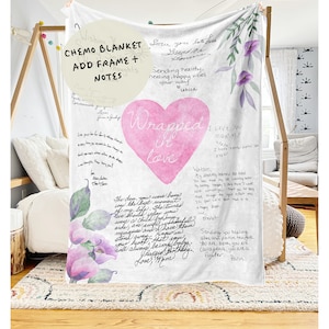 May include: A white blanket with pink watercolor flowers and a large pink heart with the words "Wrapped in love" written inside. The blanket is covered in handwritten messages of love and support.