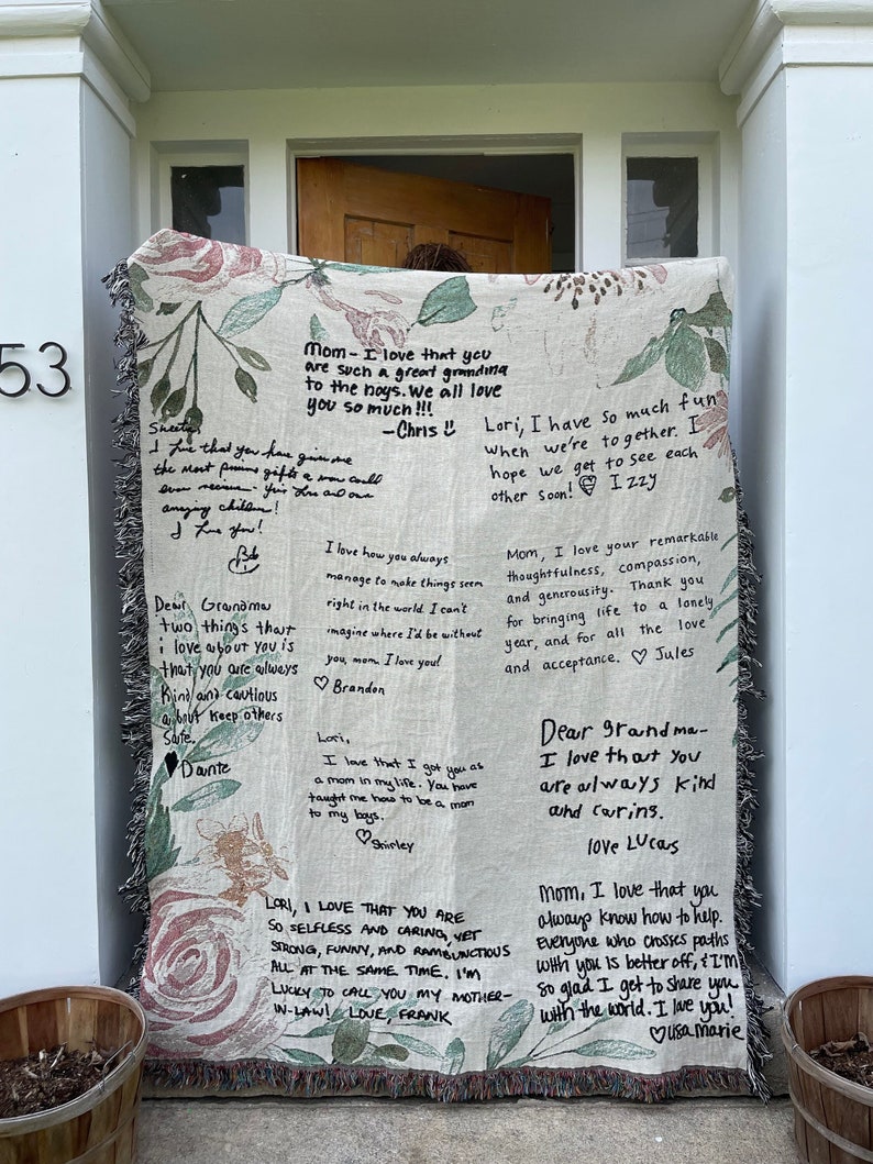 May include: A beige woven throw blanket with a floral pattern and handwritten messages of love and appreciation. The messages include "Mom - I love that you are such a great grandma to the boys. We all love you so much!!! -Chris L" and "Dear Grandma - I love that you are always kind and caring. Love Lucas".
