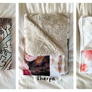 May include: Three folded blankets in different textures: woven, sherpa, and minky. The woven blanket has a colorful floral pattern, the sherpa blanket has a beige fleece texture, and the minky blanket has a white background with a pink floral pattern.