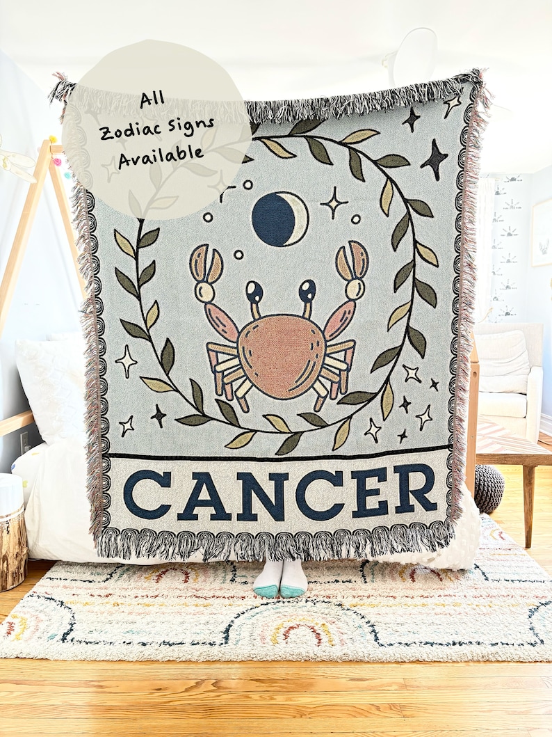 May include: A woven tapestry throw blanket with a blue background and a brown crab illustration. The blanket has a fringe border and the words "CANCER" are printed in black at the bottom. The text "All Zodiac Signs Available" is written in black on a white circle in the top left corner.