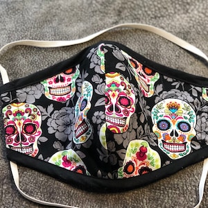 May include: A black face mask with a colorful sugar skull pattern. The mask has white elastic straps.