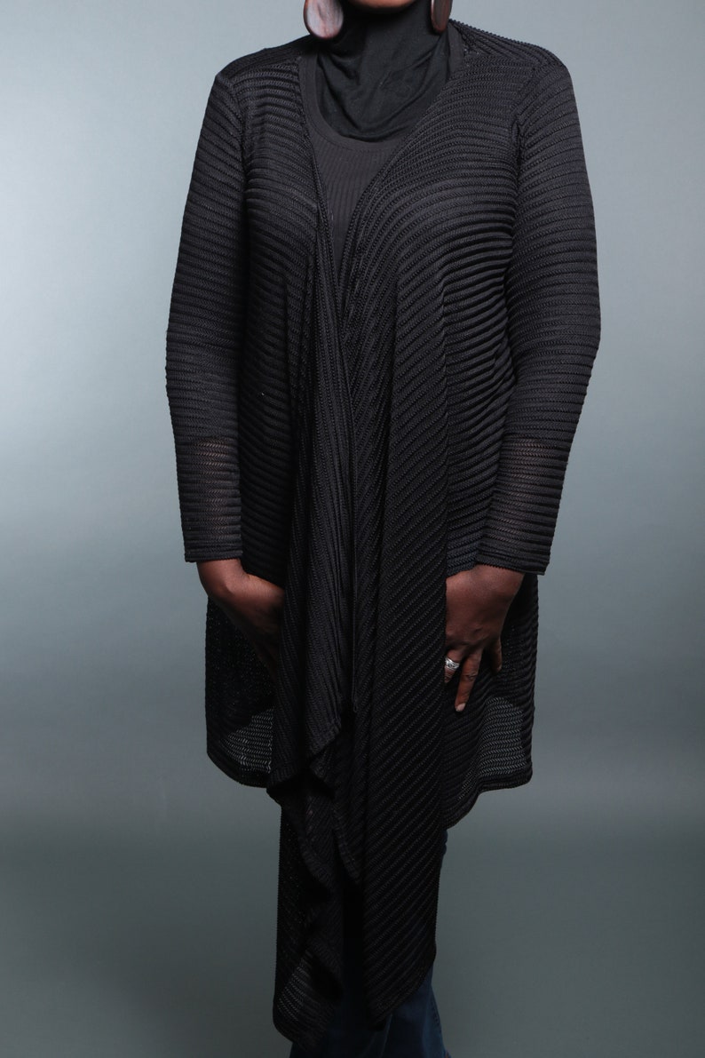 Op de afbeelding: Een zwarte open-front cardigan met een geribbelde textuur. De cardigan is gedrapeerd over een zwarte mock neck shirt en blauwe jeans.