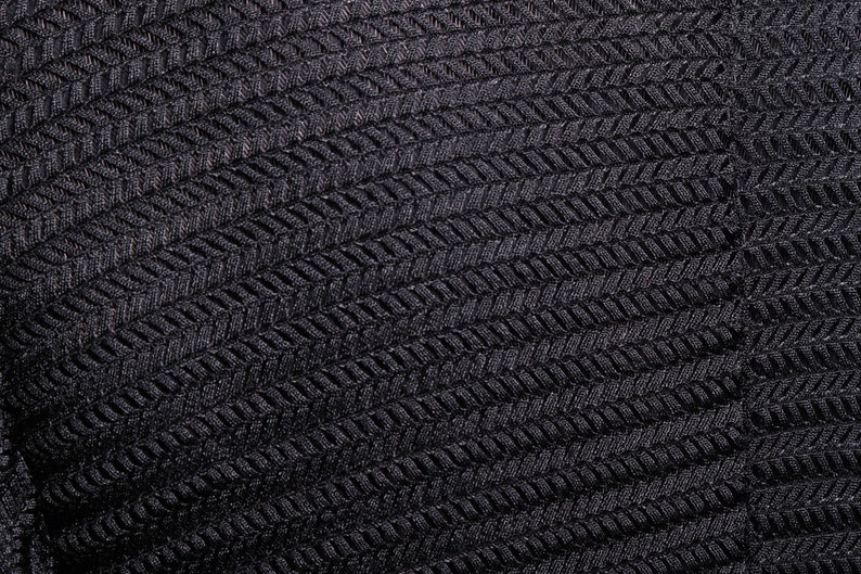 Op de afbeelding: Zwarte stof met een textuur, geweven patroon. De stof heeft een herringbone-ontwerp.