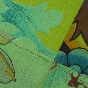 Op de afbeelding: Een patchwork stof met verschillende bloem- en geometrische patronen in tinten groen, blauw, bruin en geel. De stof is aan elkaar gestikt met zichtbare naden.