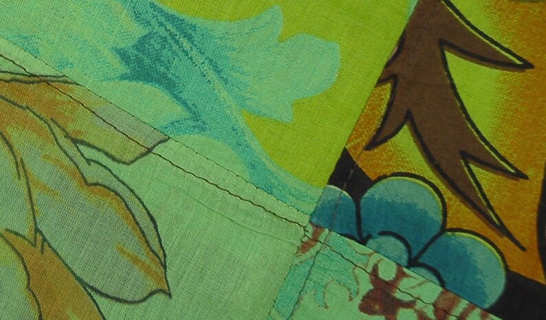 Op de afbeelding: Een patchwork stof met verschillende bloem- en geometrische patronen in tinten groen, blauw, bruin en geel. De stof is aan elkaar gestikt met zichtbare naden.