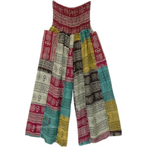 May include: Multicolored patchwork pants with an elastic waistband. The fabric features a white background with a repeating pattern of brown and black symbols.