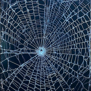 May include: A dark blue surface with a spiderweb-like pattern of cracks radiating from a central point. The cracks are thin and white, creating a web-like design across the surface.