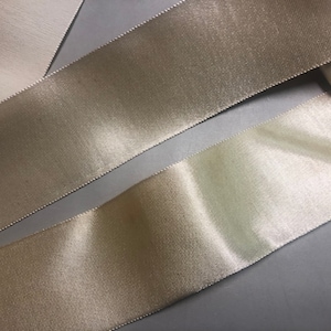 May include: Two rolls of ivory satin ribbon. The ribbon is smooth and shiny.