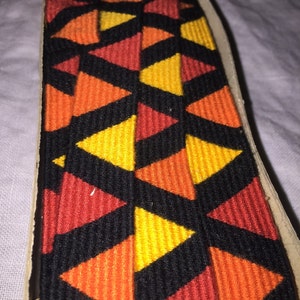 May include: A close-up of a black, orange, and yellow patterned fabric ribbon. The ribbon is made of a woven material and has a geometric design.