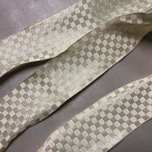 May include: A close-up of a beige and white checkered ribbon. The ribbon is woven with a subtle texture and has a satin-like finish.