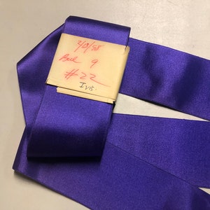 Pode incluir: Fita de cetim roxo com uma etiqueta escrita à mão que diz "3/3/58, Bulk 9, #22, Invis."