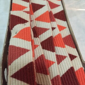 May include: A close-up of a folded fabric trim with a repeating pattern of orange, brown, and white triangles.