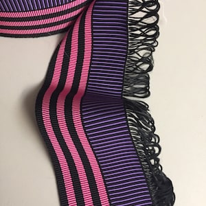 May include: Purple and pink striped ribbon with black stripes and a black fringe on one edge.