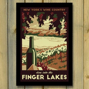 May include: A framed vintage poster promoting New York's Finger Lakes wine region. The artwork features a wine bottle, grapes, and a vineyard landscape. Text includes "New York's Wine Country" and "dive into the Finger Lakes."