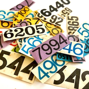 May include: A collection of rectangular paper tags featuring various printed numbers in black, blue, and yellow. The tags are scattered in a pile, displaying sequences such as 6205, 7994, 8544, 496, 342, 62, 100, 92, 865, 50, 985, 46, and 150.
