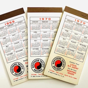 Può includere: Tre blocchi di calendario vintage, datati 1969 e 1970, con rilegatura marrone. Ogni calendario mostra le date mensili e il logo Northern Pacific Railway in rosso e nero. La parte inferiore dei calendari include il testo "Chicago - Twin Cities".
