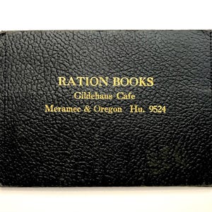 Può includere: Porta libri di razionamento in pelle nera con scritte dorate. Il testo recita "RATION BOOKS" sopra "Gildehaus Cafe" e "Meramec & Oregon Hu. 9524". La pelle ha una superficie strutturata.