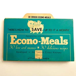 Puede incluir: Libro de cocina turquesa vintage titulado "Econo-Meals" con letras doradas y una ilustración de cerdo. La portada dice "Cómo ahorrar hasta 6,50 € al mes" y enumera 30 menús y recetas de bajo coste. También es visible el logotipo de Crisco.