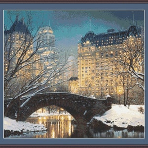 May include: A snowy winter scene in Central Park, London. A stone bridge arches over a frozen pond, with snow-covered trees and buildings in the background. The buildings are lit up with warm yellow lights, creating a cosy and festive atmosphere.