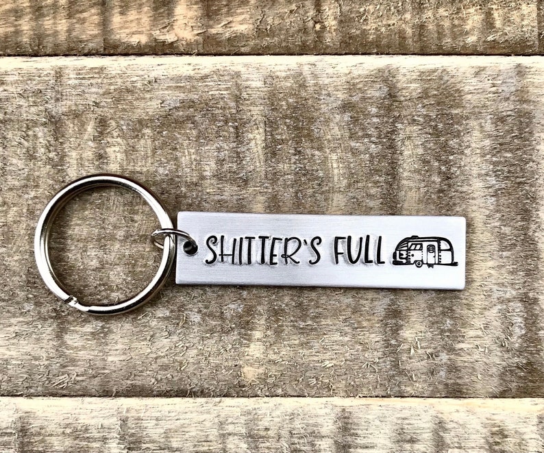 May include: Silver keychain with a camper silhouette and the text "Shitter's Full".