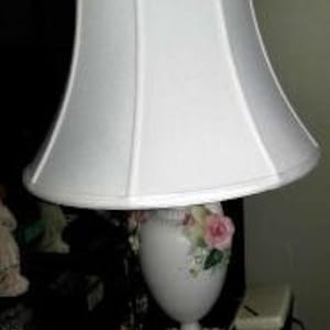 May include: White porcelain table lamp with a white lampshade. The base of the lamp is shaped like a vase with pink and white roses.