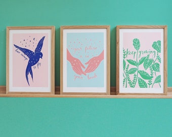 Peut inclure: Trois impressions d'art encadrées dans du bois clair. L'impression de gauche montre un oiseau bleu foncé sur fond rose avec le texte "have courage to fly". Celle du centre montre des mains roses sur fond bleu clair avec le texte "your future is in your hands". Celle de droite montre des feuilles vertes sur fond rose avec le texte "keep growing".