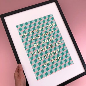May include: A framed print with a green and pink geometric pattern. The text "IN EVERY JOB THAT MUST BE DONE THERE IS AN ELEMENT OF FUN" is printed in gold letters.
