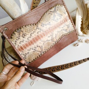 May include: A brown leather clutch with a snakeskin pattern and gold studs. The clutch has a long brown strap.
