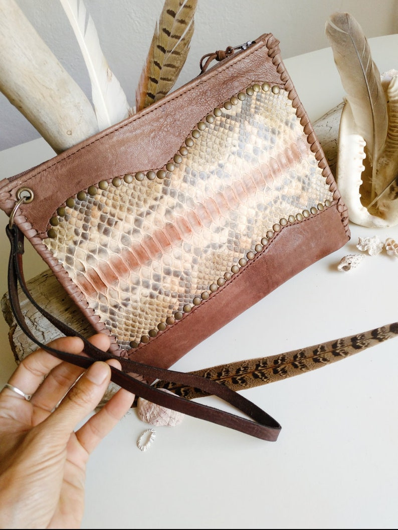 May include: A brown leather clutch with a snakeskin pattern and gold studs. The clutch has a long brown strap.