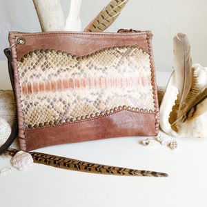 May include: A brown leather clutch with a snakeskin pattern and gold accents. The clutch has a zipper closure and a long strap.