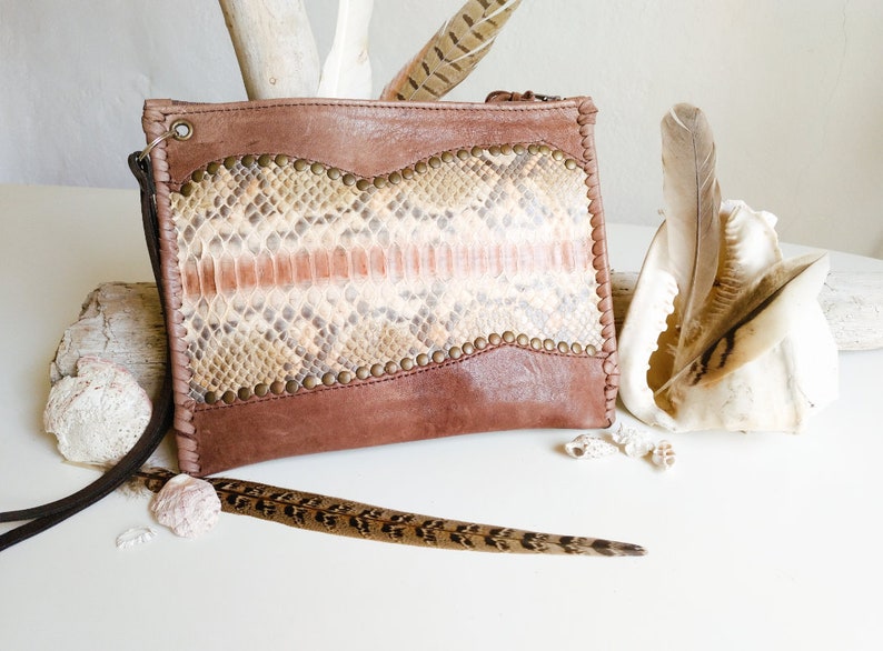 May include: A brown leather clutch with a snakeskin pattern and gold accents. The clutch has a zipper closure and a long strap.