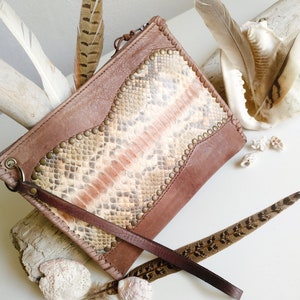 May include: A brown leather clutch with a snakeskin pattern and metal studs. The clutch has a long brown strap.