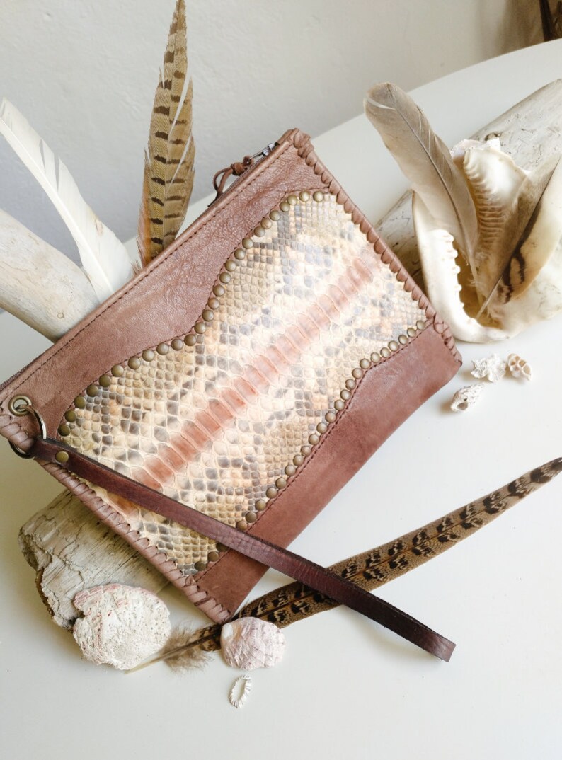 May include: A brown leather clutch with a snakeskin pattern and metal studs. The clutch has a long brown strap.