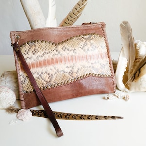 Könnte beinhalten: Eine braune Lederclutch mit Schlangenhautmuster und einem langen Riemen. Die Clutch hat einen Klappverschluss und ist mit Metallnieten verziert.