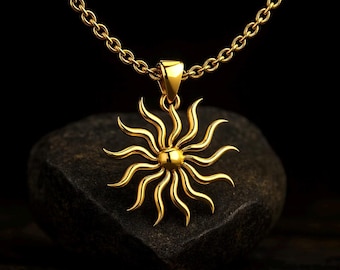 May include: Gold-colored sun pendant necklace. The pendant features a detailed sun design with radiating rays and a central sphere. The necklace chain is also gold-colored, and the pendant is displayed against a dark background.