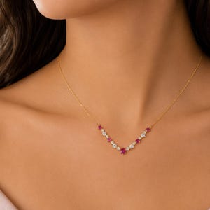 May include: A delicate gold chain necklace featuring a V-shaped pendant arrangement. The pendant consists of alternating round-cut vibrant red rubies and clear white diamonds, set in a symmetrical pattern that follows the V-shape of the chain.